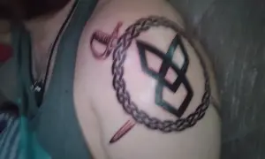 Tatuaż na ramieniu: symbol odrodzenia, spleciony łańcuch, szabla i sztylet.