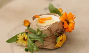 Selbstgemachte Ringelblumensalbe in einem Becher, verziert mit frischen Ringelblumen und Blättern.
