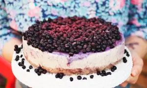 Ein köstlicher Blueberry Cheesecake, üppig belegt mit frischen Blaubeeren, wird auf einem weißen Tortenständer präsentiert.