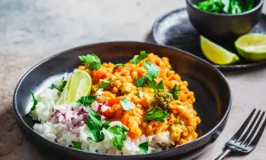Un plat de riz blanc garni d'un curry de lentilles corail et légumes, parsemé de coriandre fraîche et de quartiers de citron vert. Une recette d'été parfaite.