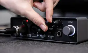 Dłoń kręci gałką miksera audio, regulując poziom sygnału. Widoczne złącza audio i wejścia mikrofonowe.
