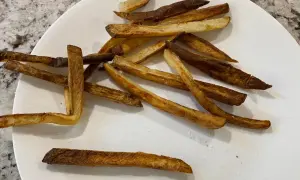 En tallrik med krispiga pommes frites, perfekt tillagade i airfryer. Saltkorn glittrar på de gyllene pommes.