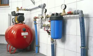 System hydroforowy: czerwony zbiornik, pompa, niebieski filtr wody i manometry. To rozwiązanie zapewnia stałe ciśnienie wody.