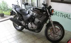 Czarny motocykl Honda z widocznym silnikiem i wydechem, gotowy do jazdy. Obok stoi rower.