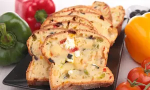 Tranches d'un cake savoureux aux olives et feta, entouré de poivrons colorés et de tomates.