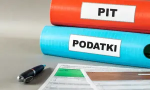 Dwa segregatory, jeden czerwony z napisem "PIT", drugi niebieski z napisem "PODATKI", leżą na dokumentach podatkowych.