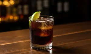 Ett glas rom och cola med is och lime på en träbar.