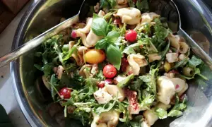 Pyszna sałatka tortellini z rukolą, pomidorkami koktajlowymi, oliwkami i serem feta. Idealna na letnie przyjęcie.