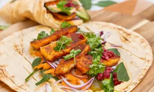 En läcker halloumi wrap med hummus, rivna morötter, rödlök och färska örter. En annan wrap syns i bakgrunden.