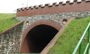 Akwedukt w Fojutowie, z ceglanym łukiem i kamiennym murem, otoczony zielenią.