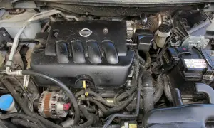 Silnik Nissan Qashqai J10, widok z góry. Czarna pokrywa silnika z logo Nissan, alternator, akumulator i przewody.