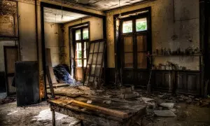 Intérieur d'un lieu abandonné en France. Un vieux bureau en bois trône au milieu des débris, sous des ampoules nues.
