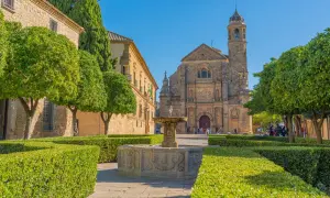 Fuente renacentista en plaza de Úbeda y Baeza, con iglesia barroca al fondo y árboles frutales.