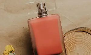 Perfumy Lancome Oui w koralowym odcieniu, obok suszonej róży i plastra drewna.