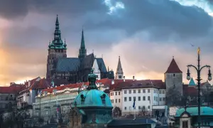 Prag dom mit seinen Türmen und Dächern unter dramatischem Himmel. Ein Vogel fliegt über die historische Kulisse.