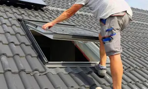 Pracownik montuje okno dachowe. Zastanawiasz się, ile kosztuje okno dachowe? Sprawdź ceny!
