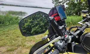 Lusterko motocyklowe z odbiciem drzew i telefonem nawigacyjnym na kierownicy, nad jeziorem.