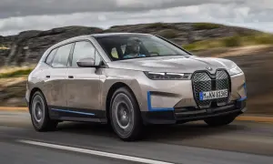 Złoty BMW iX jedzie po drodze, otoczony skalistym krajobrazem.