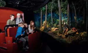 Familj i en vagn på ett vikingamuseum i Sverige, tittar på en dramatisk scen med vikingar i en skog.