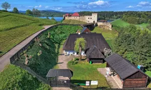 Widok z lotu ptaka na skansen z zamkiem, jeziorem i zielonymi wzgórzami.