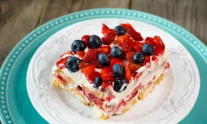 Tranche de tiramisu aux fruits rouges, fraises et myrtilles, sur une assiette blanche ornée, posée sur une assiette turquoise.