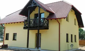 Jasnożółty dom z czerwonym dachem i drewnianym balkonem.