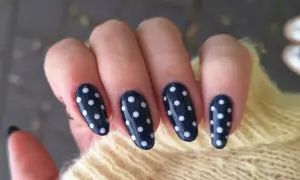 Manucure élégante avec un nail art pois sur fond bleu marine. Les ongles sont ornés de petits ronds blancs, créant un look ludique et chic.