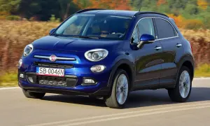 Błękitny Fiat 500X jedzie po drodze, otoczony jesienną przyrodą.