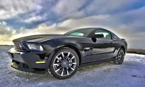 Czarny Ford Mustang GT 5.0, jeden z tych tanich sportowych aut, zaparkowany na zaśnieżonej drodze pod dramatycznym niebem.
