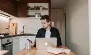 Mężczyzna w kuchni sprawdza telefon, bo Netia brak internetu uniemożliwia pracę na laptopie.