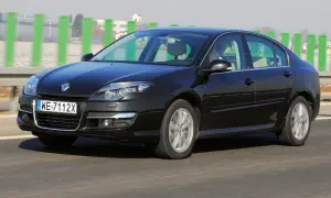 Czarny Renault Laguna 3 2.0 dCi jedzie po drodze, za zielonymi słupkami.