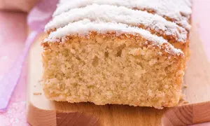 Bizcocho de coco esponjoso, cubierto con coco rallado, servido en tabla de madera.