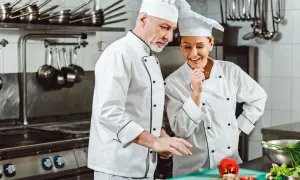 Zwei Köche in weißer Arbeitskleidung besprechen Zutaten. Das Waschen der Arbeitskleidung ist steuerlich absetzbar.