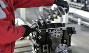Main d'un mécanicien en combinaison rouge installant un vilebrequin dans un bloc moteur. Le joint spi vilebrequin est essentiel pour l'étanchéité.