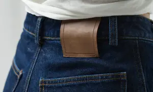 Detale ciemnych jeansów z brązową naszywką. Denim to materiał, z którego są wykonane.
