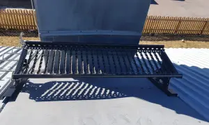 En takbrygga framför en stor ventilationsanläggning, liknande en skorsten. Solen kastar ett mönstrat skuggspel.