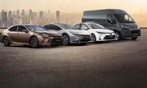 Różnorodne modele Toyota: brązowa Camry Hybrid, srebrny Prius Plug-in Hybrid, biała Corolla i szary Proace Max na tle miasta.