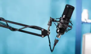 Czarny mikrofon pojemnościowy na wysięgniku, gotowy do nagrania podcastu. W tle niebieskie tło.