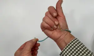 Pokazuje, jak zapiąć bransoletkę. Jedna ręka trzyma zapięcie, druga zapina je na nadgarstku.