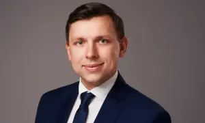 Portret mężczyzny w granatowym garniturze i krawacie na szarym tle.