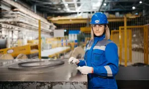 Kobieta w niebieskim kasku i okularach ochronnych, pracująca w hali produkcyjnej. Dba o BHP, co to znaczy? Bezpieczeństwo i higiena pracy.