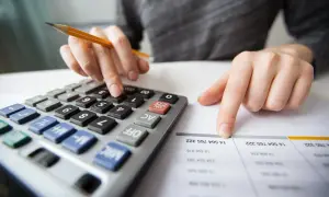Mani che usano una calcolatrice rigo e25 730 e un foglio con numeri.