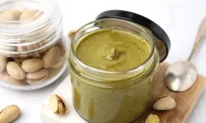 Słoik z kremowym, zielonym kremem pistacjowym, obok którego leżą łuskane pistacje. Idealny do włoski krem pistacjowy przepis.