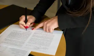 Kobieta z czerwonymi paznokciami podpisuje dokument, który może być wnioskiem o zmianę w księdze wieczystej.