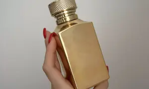 Złota butelka luksusowych perfum w dłoni z czerwonymi paznokciami. Elegancki flakon, który kusi zapachem.