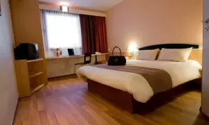 Pokój w Ibis Hotel Zabrze: łóżko, toaletka z laptopem, szafa z telewizorem i okno z zasłonami.