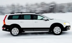 Vit Volvo XC70 kör på en snöig väg, med en förare bakom ratten. Bilen är i rörelse, vilket skapar en suddig bakgrund av träd.