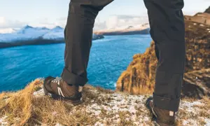 Nogi w butach trekkingowych na tle błękitnego morza i ośnieżonych gór. To prawdziwy hiking po polsku, pełen przygód i pięknych widoków.