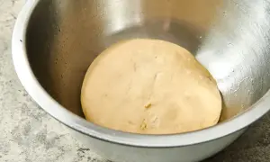 Gładkie, jasne ciasto na pizzę w metalowej misce, gotowe do wyrastania.