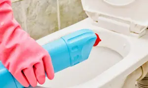 Mano con guanto rosa usa detergente per pulire il water incrostato.